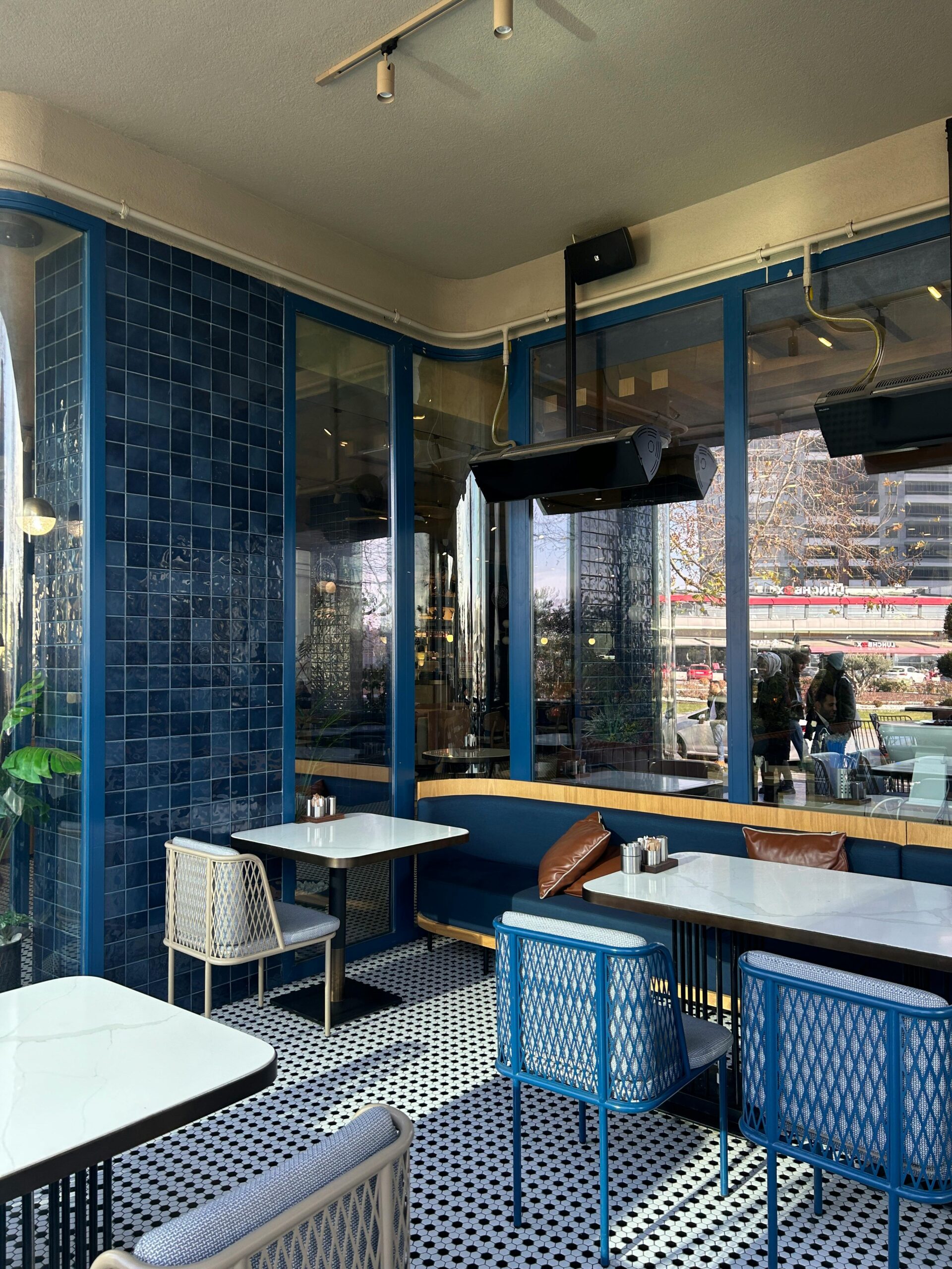 A chic cafe with blue tiles and large windows, offering an inviting and sunny space for diners.